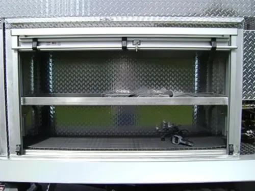 Exterior view of small fire truck showing cab, body compartments, and wheel/tire area.