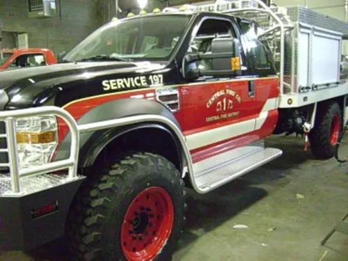 Exterior view of small fire truck showing cab, body compartments, and wheel/tire area.