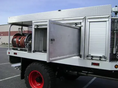 Exterior view of small fire truck showing cab, body compartments, and wheel/tire area.