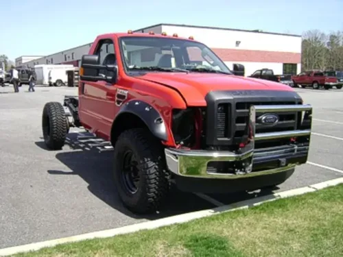 Exterior view of small fire truck showing cab, body compartments, and wheel/tire area.