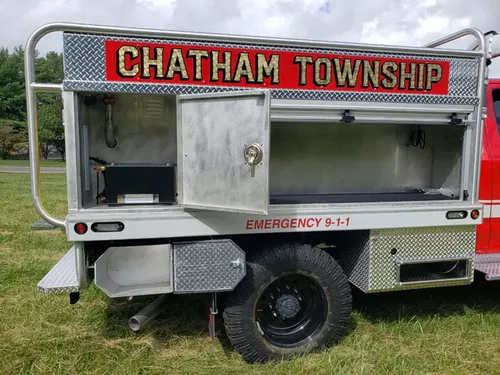 Exterior view of small fire truck showing cab, body compartments, and wheel/tire area.