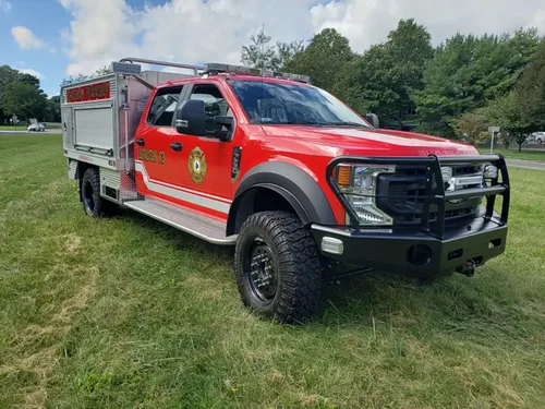 Exterior view of small fire truck showing cab, body compartments, and wheel/tire area.