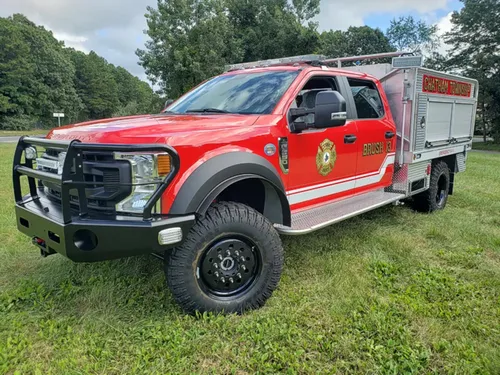 Exterior view of small fire truck showing cab, body compartments, and wheel/tire area.