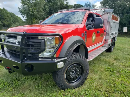Exterior view of small fire truck showing cab, body compartments, and wheel/tire area.