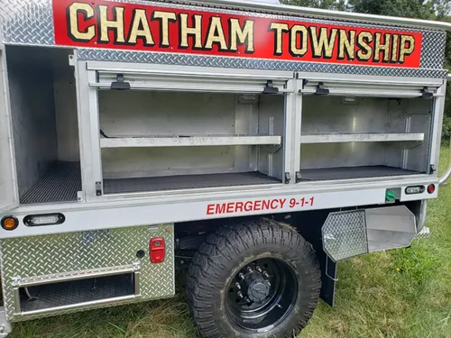 Exterior view of small fire truck showing cab, body compartments, and wheel/tire area.