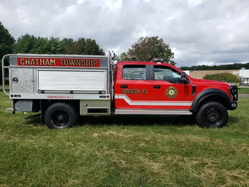 Exterior view of small fire truck showing cab, body compartments, and wheel/tire area.
