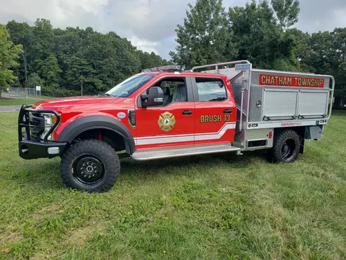 Exterior view of small fire truck showing cab, body compartments, and wheel/tire area.
