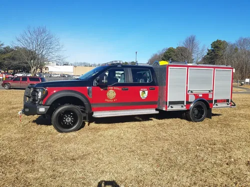 Exterior view of small fire truck showing cab, body compartments, and wheel/tire area.