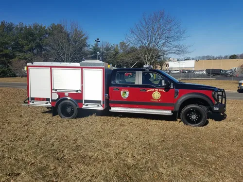 Exterior view of small fire truck showing cab, body compartments, and wheel/tire area.