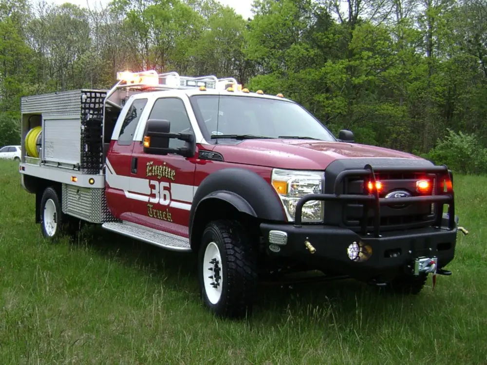 Exterior view of small fire truck showing cab, body compartments, and wheel/tire area.