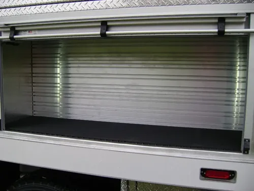 Exterior view of small fire truck showing cab, body compartments, and wheel/tire area.