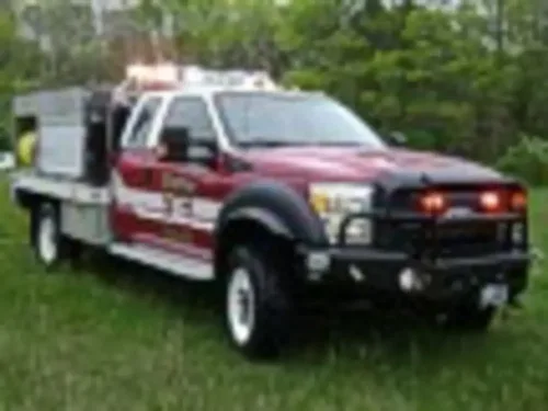 Exterior view of small fire truck showing cab, body compartments, and wheel/tire area.