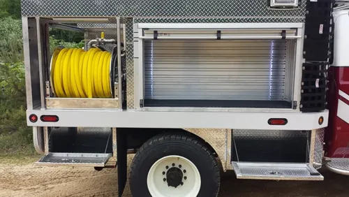 Exterior view of small fire truck showing cab, body compartments, and wheel/tire area.