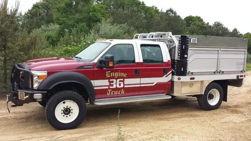 Exterior view of small fire truck showing cab, body compartments, and wheel/tire area.