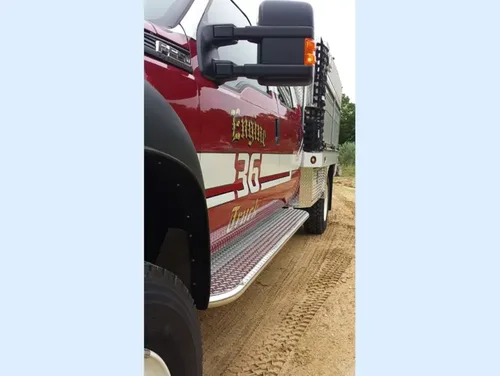 Exterior view of small fire truck showing cab, body compartments, and wheel/tire area.