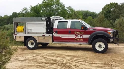 Exterior view of small fire truck showing cab, body compartments, and wheel/tire area.
