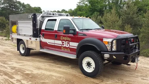 Exterior view of small fire truck showing cab, body compartments, and wheel/tire area.