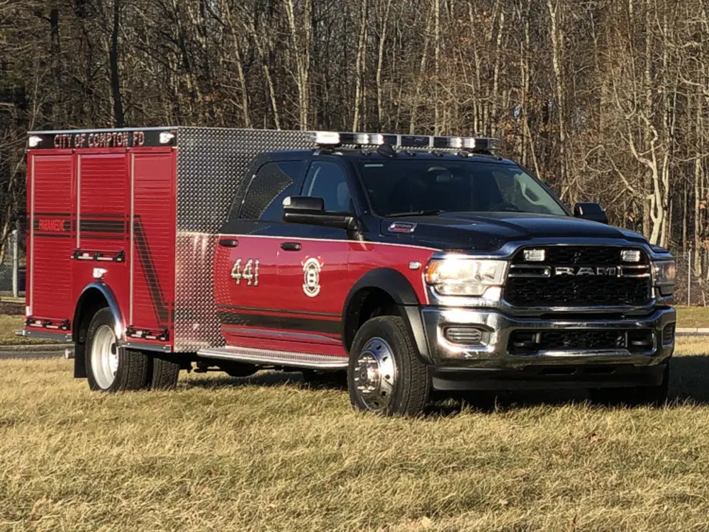 Exterior view of small fire truck showing cab, body compartments, and wheel/tire area.