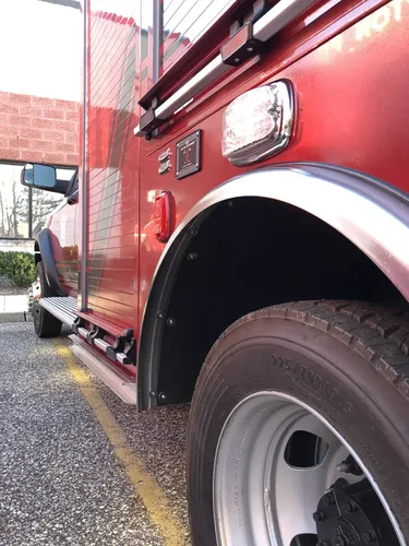 Exterior view of small fire truck showing cab, body compartments, and wheel/tire area.