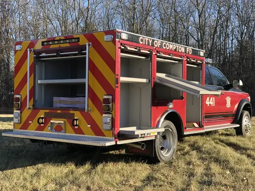 Exterior view of small fire truck showing cab, body compartments, and wheel/tire area.