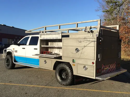 Exterior view of small fire truck showing cab, body compartments, and wheel/tire area.