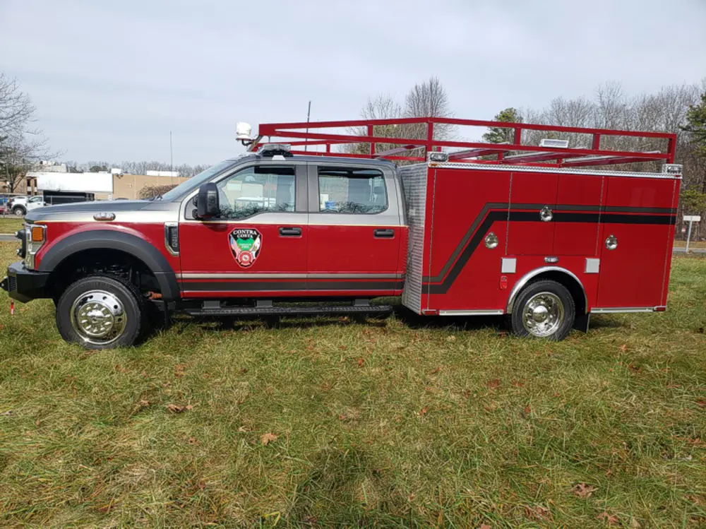Exterior view of small fire truck showing cab, body compartments, and wheel/tire area.
