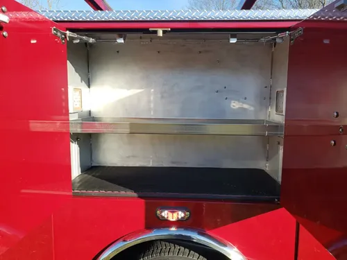 Exterior view of small fire truck showing cab, body compartments, and wheel/tire area.