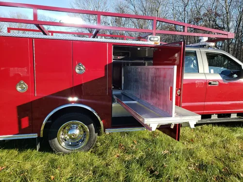 Exterior view of small fire truck showing cab, body compartments, and wheel/tire area.