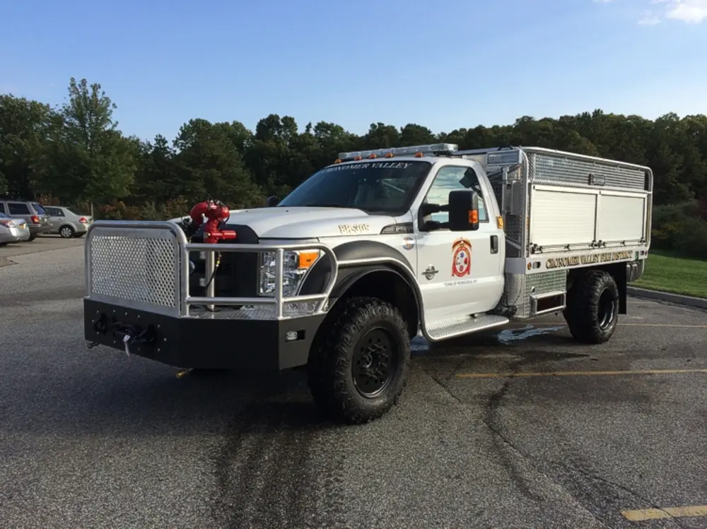 Exterior view of small fire truck showing cab, body compartments, and wheel/tire area.