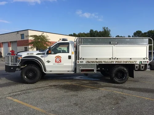 Exterior view of small fire truck showing cab, body compartments, and wheel/tire area.