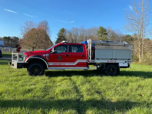 Exterior view of small fire truck showing cab, body compartments, and wheel/tire area.