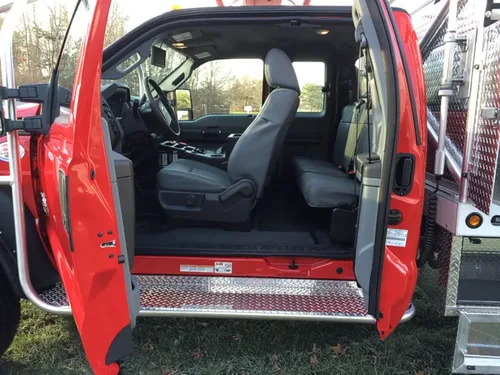 Exterior view of small fire truck showing cab, body compartments, and wheel/tire area.