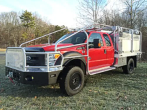 Exterior view of small fire truck showing cab, body compartments, and wheel/tire area.