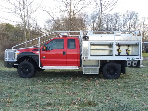 Exterior view of small fire truck showing cab, body compartments, and wheel/tire area.