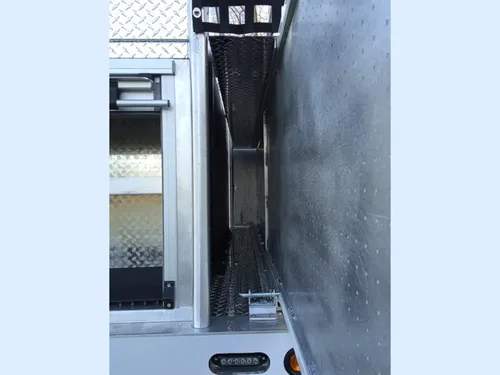 Exterior view of small fire truck showing cab, body compartments, and wheel/tire area.