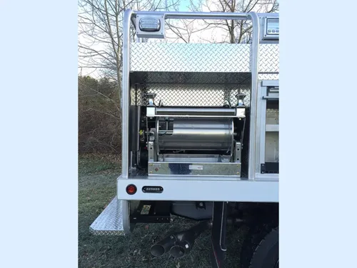 Exterior view of small fire truck showing cab, body compartments, and wheel/tire area.