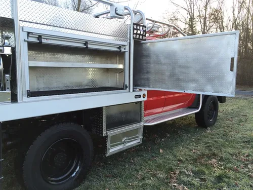 Exterior view of small fire truck showing cab, body compartments, and wheel/tire area.
