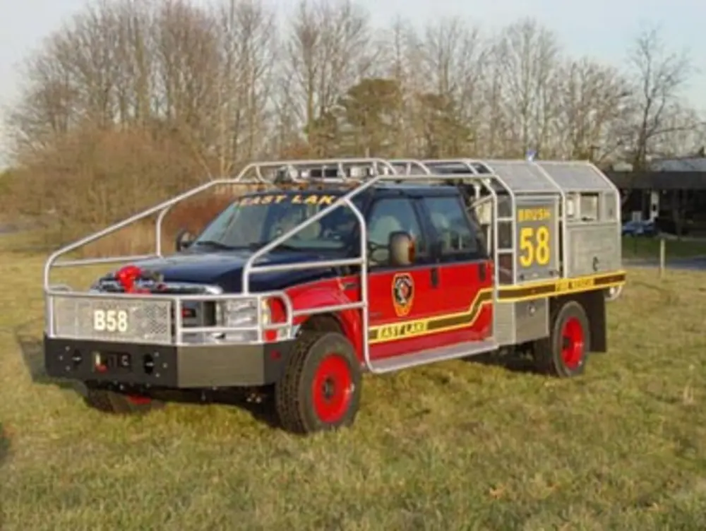 Exterior view of small fire truck showing cab, body compartments, and wheel/tire area.