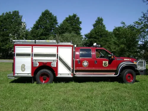Exterior view of small fire truck showing cab, body compartments, and wheel/tire area.
