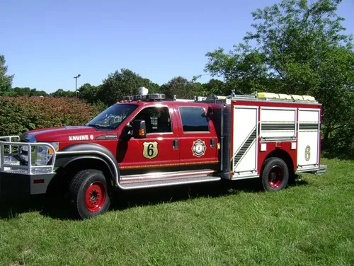 Exterior view of small fire truck showing cab, body compartments, and wheel/tire area.
