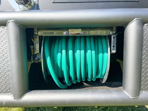 Recessed hose reel compartment with green hose coiled inside.
