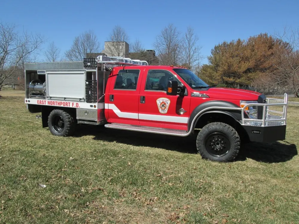 Exterior view of small fire truck showing cab, body compartments, and wheel/tire area.