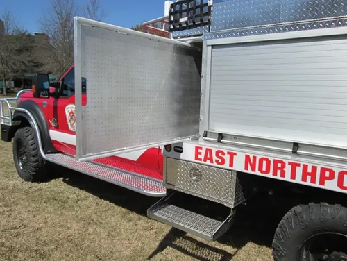 Exterior view of small fire truck showing cab, body compartments, and wheel/tire area.