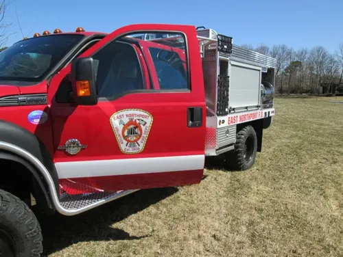 Exterior view of small fire truck showing cab, body compartments, and wheel/tire area.
