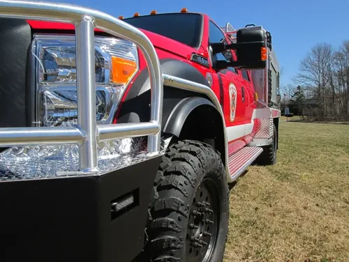 Exterior view of small fire truck showing cab, body compartments, and wheel/tire area.