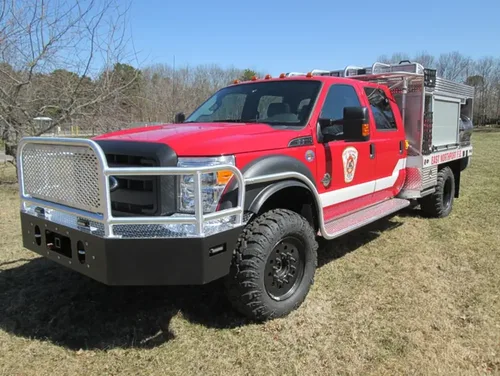 Exterior view of small fire truck showing cab, body compartments, and wheel/tire area.