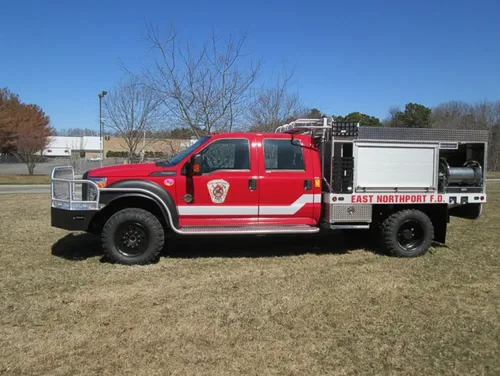Exterior view of small fire truck showing cab, body compartments, and wheel/tire area.