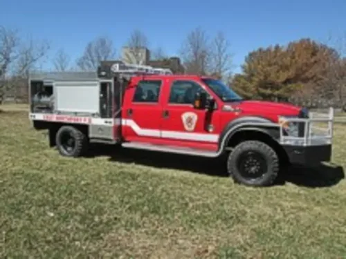 Exterior view of small fire truck showing cab, body compartments, and wheel/tire area.