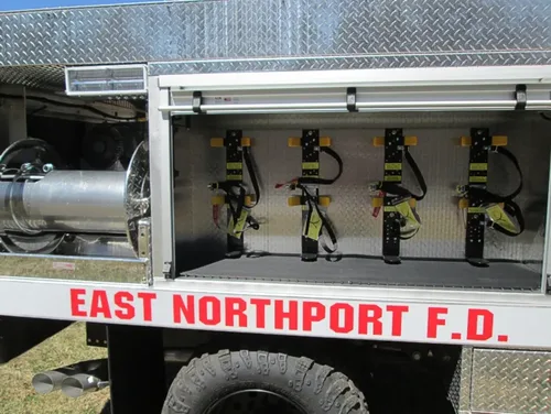 Exterior view of small fire truck showing cab, body compartments, and wheel/tire area.