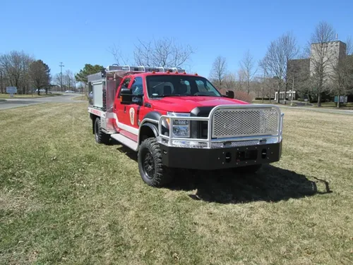Exterior view of small fire truck showing cab, body compartments, and wheel/tire area.